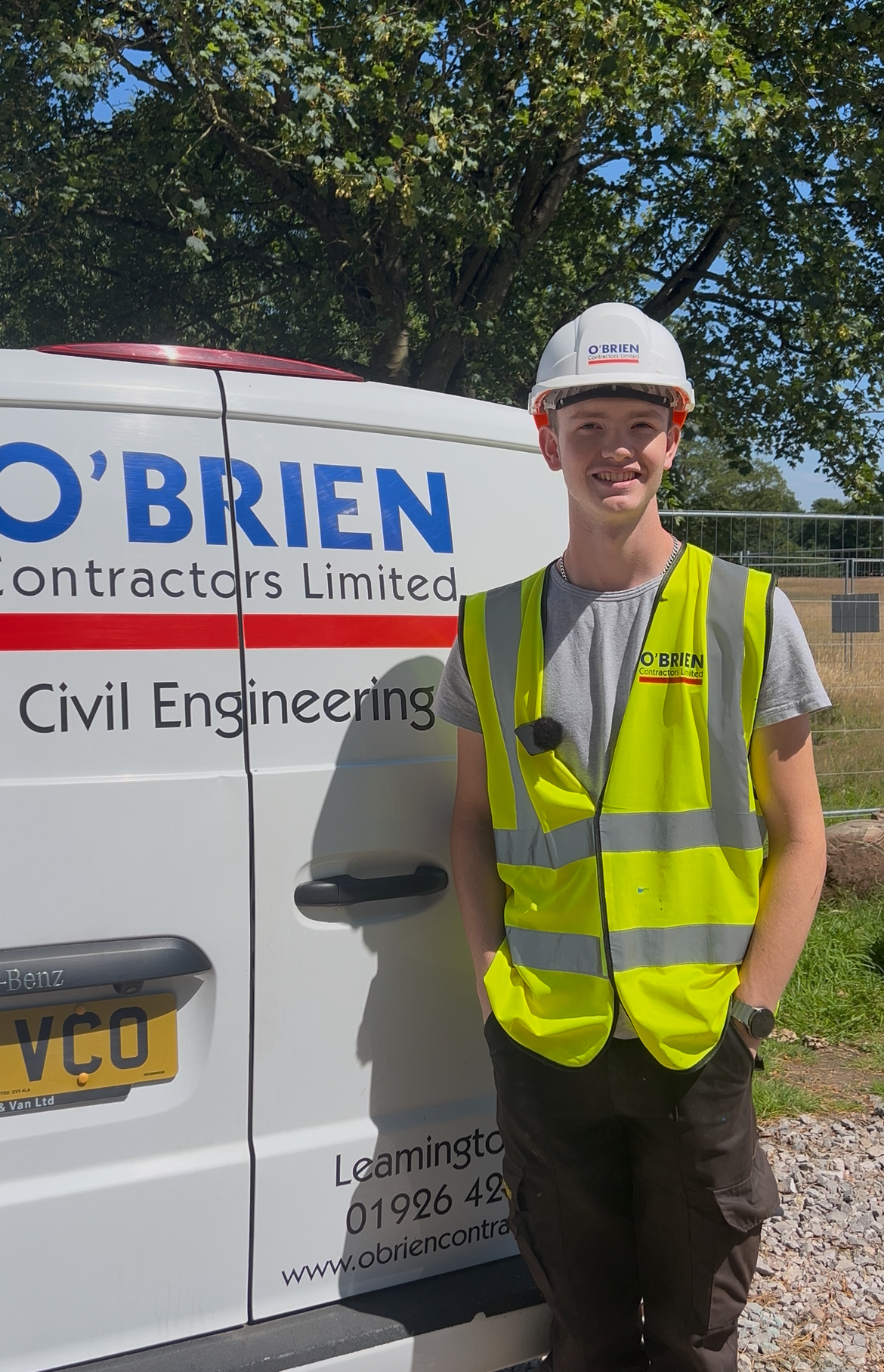 Apprentice stands in front of an O'Brien Contractors van. He is wearing a hard hat and high-vis.